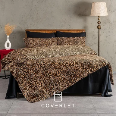 روتختی پلنگی کاوری مدل Panthera روی تخت در نمای کامل، با طرح پلنگی گرم و جسورانه، روبالشی‌های هماهنگ، ملحفه تیره و چیدمان لوکس اتاق خواب با پس‌زمینه دیوار طوسی و دکور چوبی