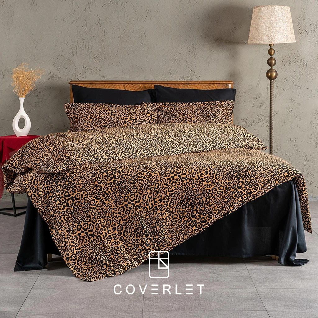 روتختی پلنگی کاوری مدل Panthera روی تخت در نمای کامل، با طرح پلنگی گرم و جسورانه، روبالشیهای هماهنگ، ملحفه تیره و چیدمان لوکس اتاق خواب با پسزمینه دیوار طوسی و دکور چوبی