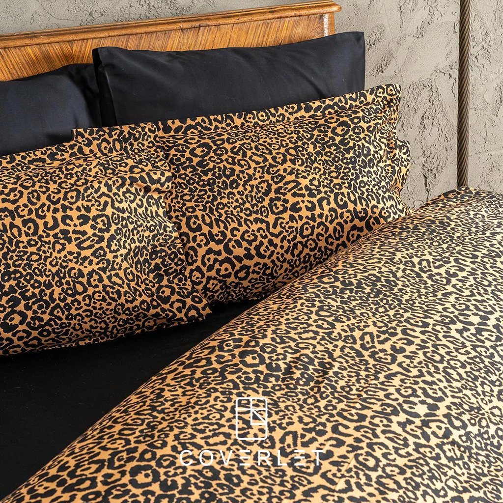 روتختی پلنگی کاوری مدل Panthera روی تخت در نمای کامل، با طرح پلنگی گرم و جسورانه، روبالشیهای هماهنگ، ملحفه تیره و چیدمان لوکس اتاق خواب با پسزمینه دیوار طوسی و دکور چوبی